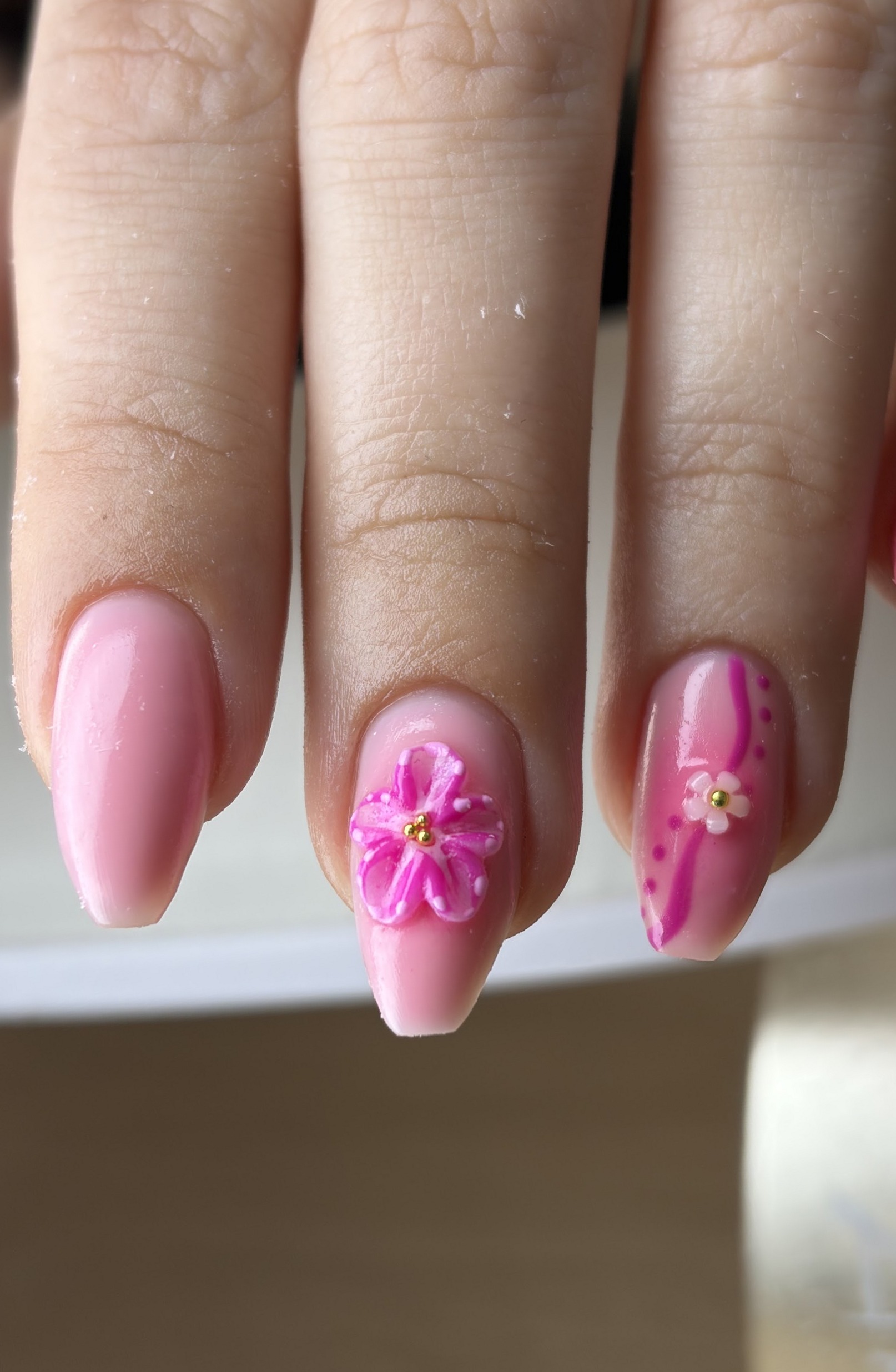 Lichtroze amandelnagels, een met een roze 3D-bloem en een met roze stipjes